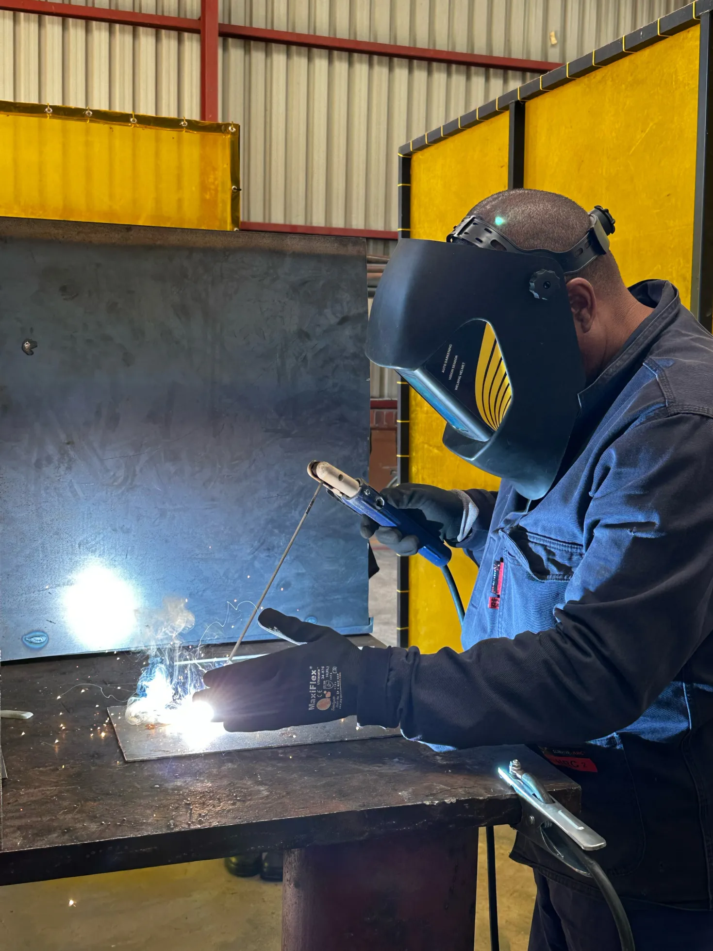 Our welding Facilitator in overalls welding some metal with bright flash from the welding machine 
